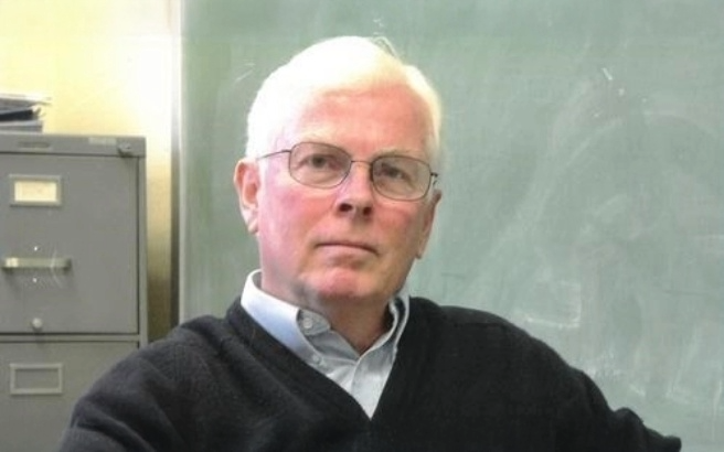 Photo of Dr. John McNamara sitting in front of a chalboard