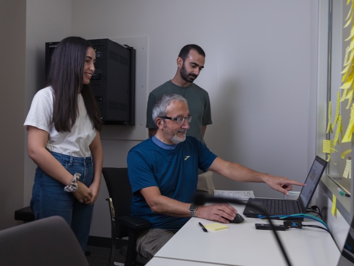pavlidis sits with students around him looking at a laptop
